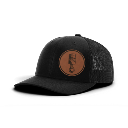 Trucker hat with angry piston patch, dark charcoal front and black mesh back panels.