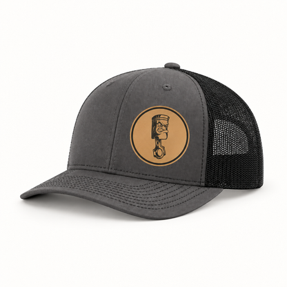 Dark gray trucker hat with black mesh back and round angry piston patch on front.