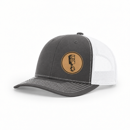 Gray trucker hat with white mesh back and round angry piston patch on front.