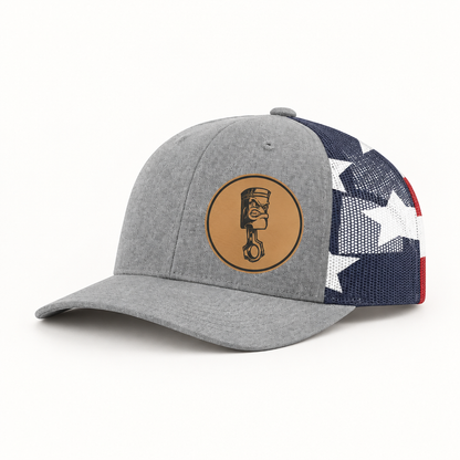Light gray trucker hat with navy/white/red star mesh side and round angry piston patch.