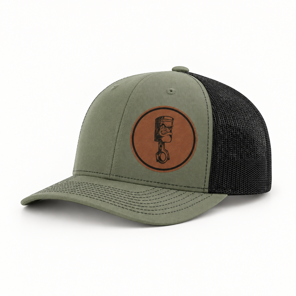 Olive-gray trucker hat with dark mesh back and round angry piston patch on front.
