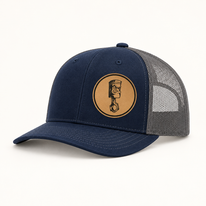 Navy trucker hat with gray mesh back and round angry piston patch on front.