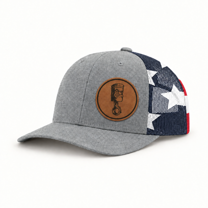 Light gray trucker hat with navy/white/red star mesh side and round angry piston patch.