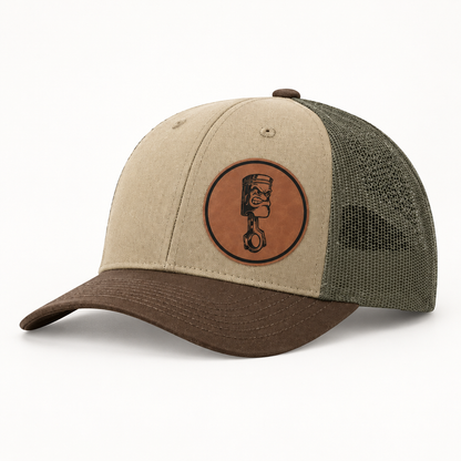Beige canvas trucker hat with olive mesh back and round Angry Piston patch