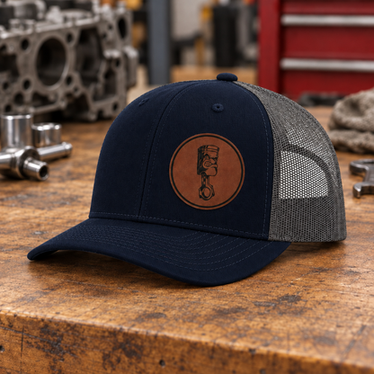 Navy and gray trucker cap with curved brim and round angry piston emblem patch