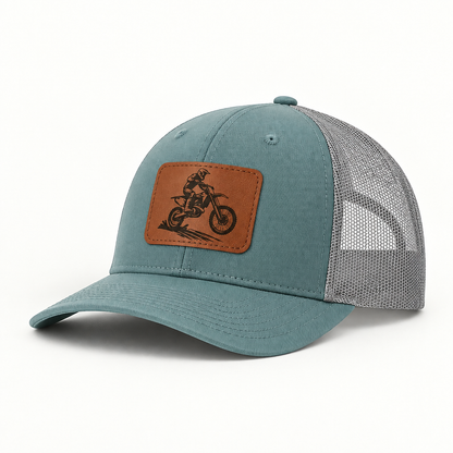 Trucker hat in teal with gray mesh; dirt bike rider patch in tan leather on front.