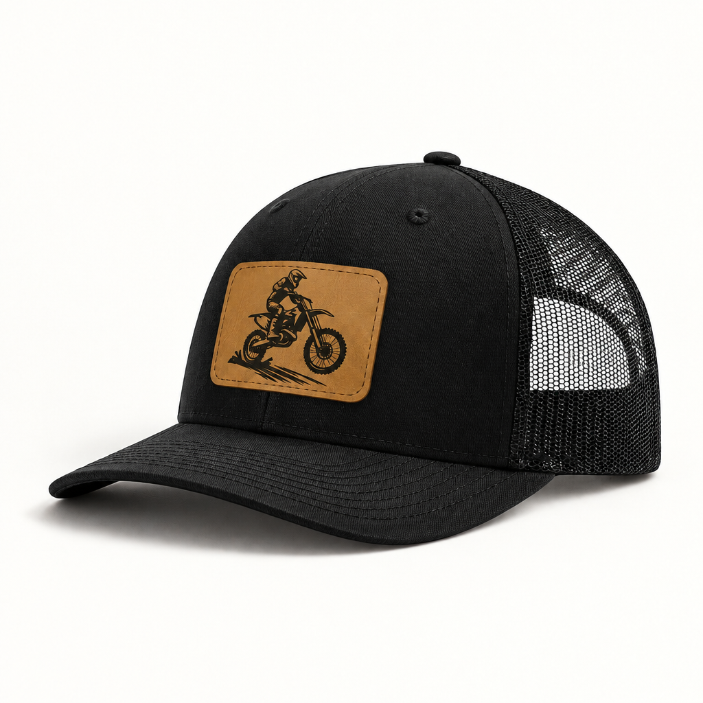 Trucker hat in black with black mesh; tan leather patch features a dirt bike rider.