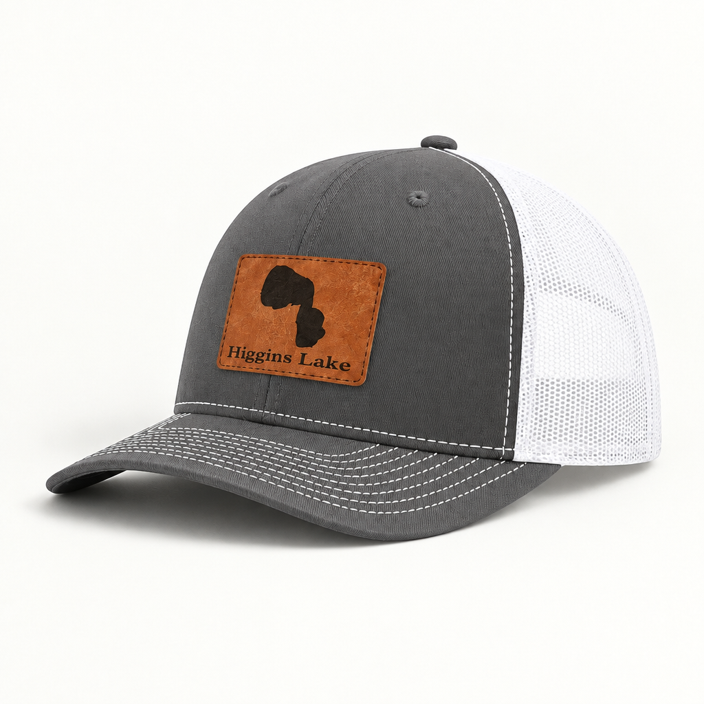 Dark gray trucker hat with white mesh back and tan patch, adjustable curved brim