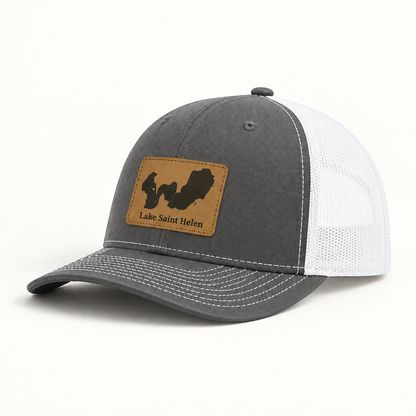 Dark gray trucker hat with tan logo patch, white mesh back, curved brim, snap button