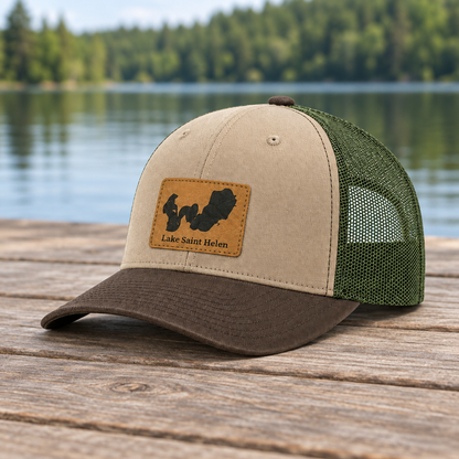 Trucker hat with tan crown and brim, green mesh sides, front logo patch
