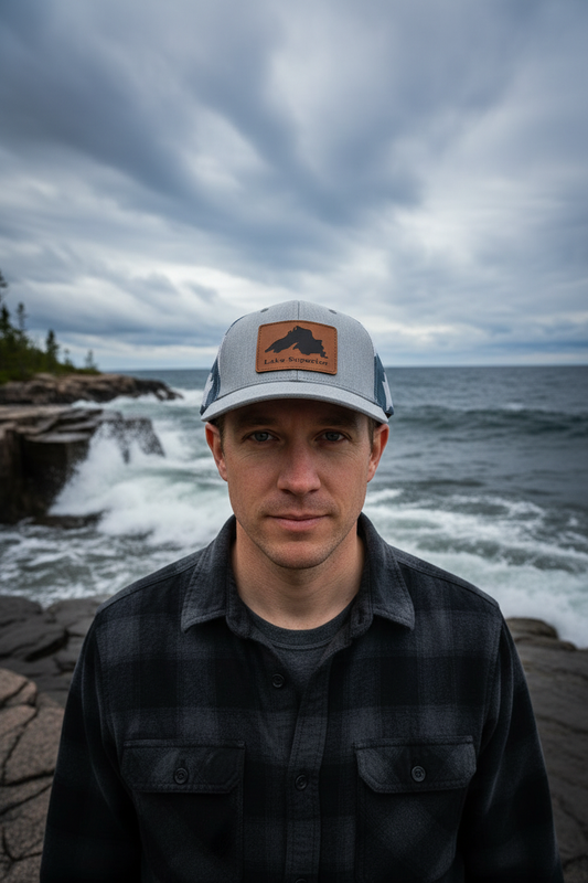 Lake Superior leatherette patch trucker hat worn by model on rugged Lake Superior shoreline with rocky coast – Keeko Designs