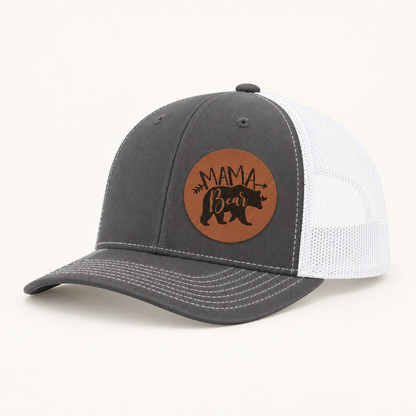 Charcoal and white trucker hat with tan “Mama Bear” patch and curved brim.