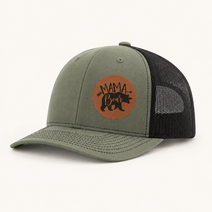 Olive green and black trucker hat with tan “Mama Bear” patch, front view.