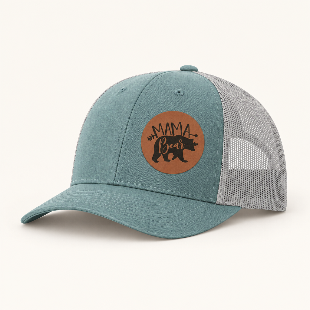 Teal trucker hat with tan “Mama Bear” patch and gray mesh side panels.