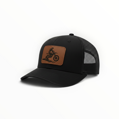 Black trucker hat with tan leather-look dirt bike patch on front.