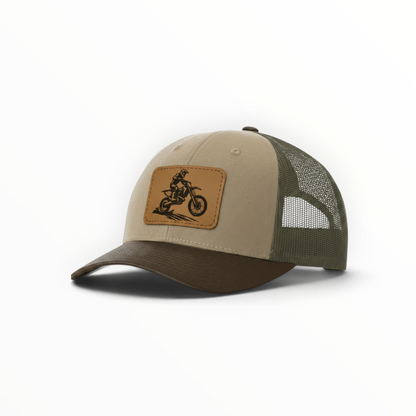 Beige and dark green trucker hat with dirt bike patch on front.